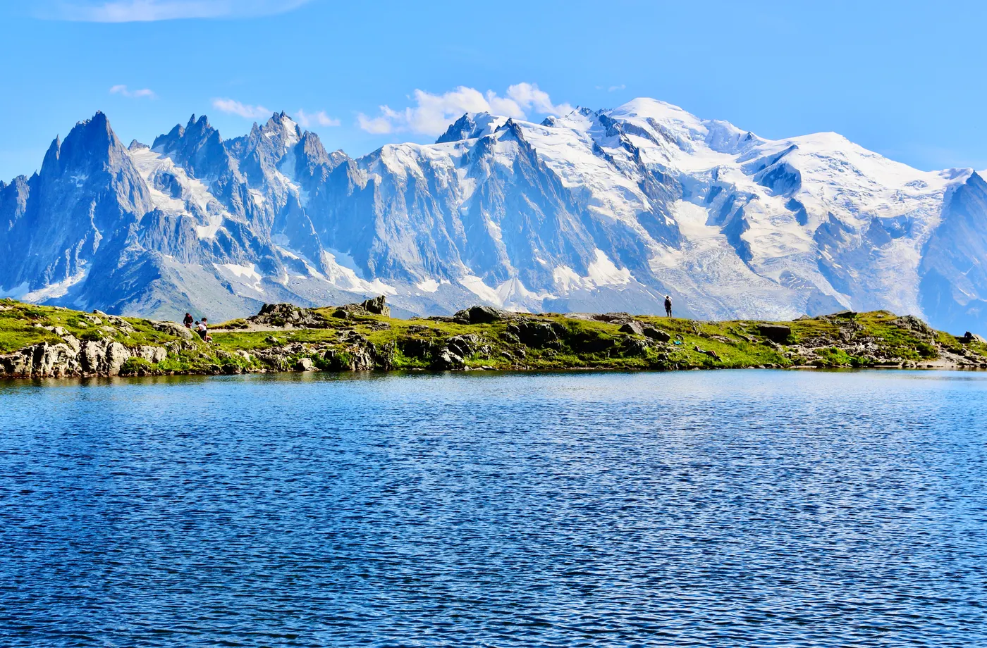 Vue à couper le souffle des sommets enneigés du Mont Blanc réfléchis dans un lac pur sous un ciel bleu éclatant.