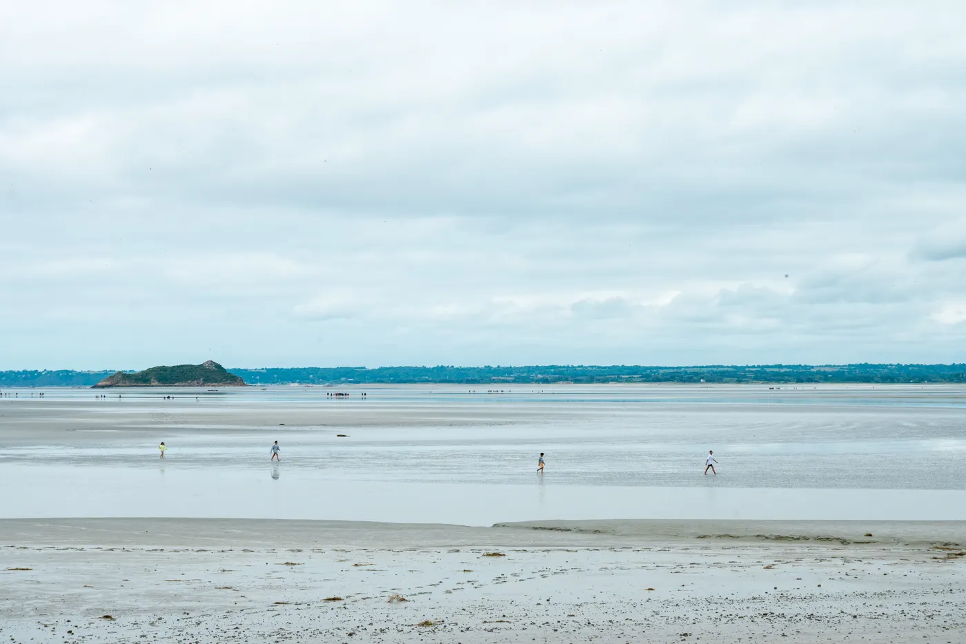 Vue panoramique des plages à marée basse du Mont-Saint-Michel, en Normandie, avec des promeneurs au loin.